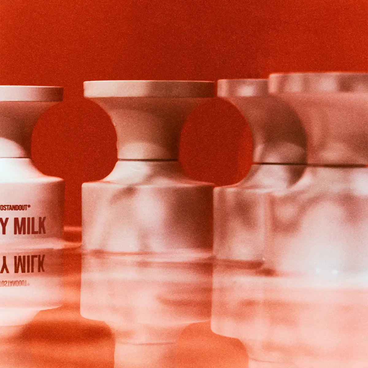 BORNTOSTANDOUT - Dirty Milk zeigt weiße Flakons mit markanter Schrift und unscharfer Spiegelung vor rotem Hintergrund