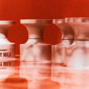 BORNTOSTANDOUT - Dirty Milk zeigt weiße Flakons mit markanter Schrift und unscharfer Spiegelung vor rotem Hintergrund