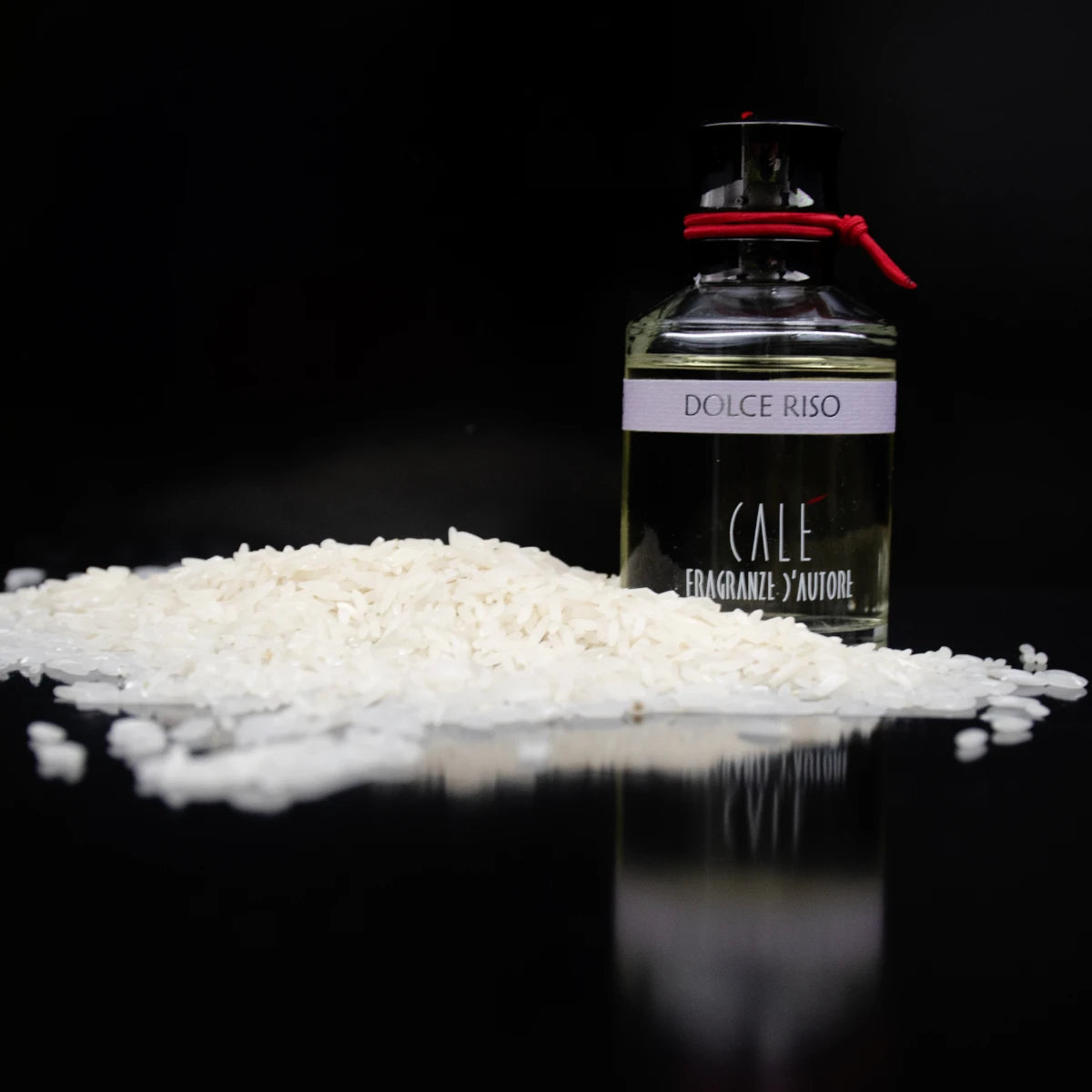Calé Fragranze d'Autore - Dolce Riso Parfumflakon mit rotem Band neben weißem Reis vor schwarzem Hintergrund