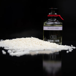 Calé Fragranze d'Autore - Dolce Riso Parfumflakon mit rotem Band neben weißem Reis vor schwarzem Hintergrund