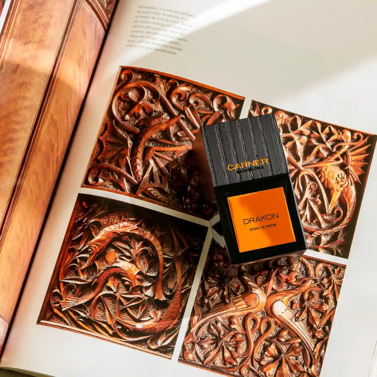 Carner Barcelona - Bestial Collection - Drakon Parfumflakon mit schwarzem Korpus und orangefarbenem Label auf kunstvollem Buchseite