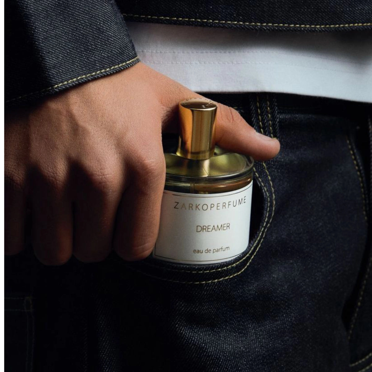 Zarkoperfume - Dreamer Parfumflakon mit goldfarbenem Verschluss in Hand vor dunkler Jeans und weißem Shirt