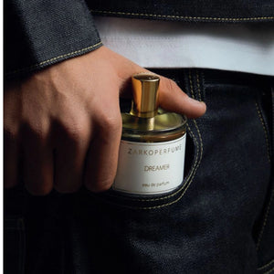 Zarkoperfume - Dreamer Parfumflakon mit goldfarbenem Verschluss in Hand vor dunkler Jeans und weißem Shirt