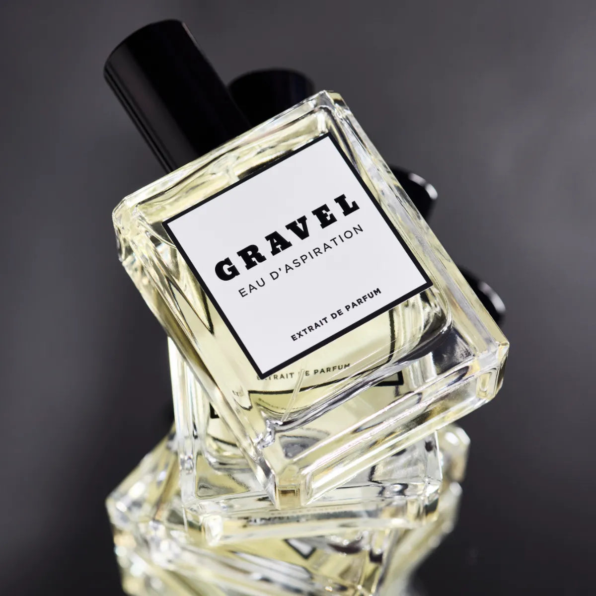 Gravel - Eau D'Aspiration Parfumflakon mit klarem Glas und schwarzem Verschluss vor dunklem Hintergrund