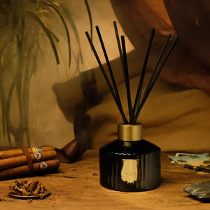 Trudon - Reed Diffusor - Ernesto mit schwarz geriffeltem Flakon und goldfarbenem Verschluss auf rustikalem Holztisch in warmem Licht