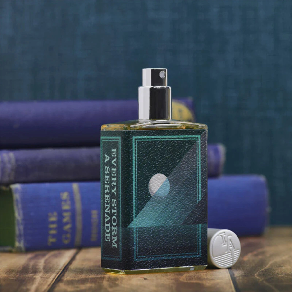Imaginary Authors - Every Storm a Serenade 2nd Edition Parfumspray mit dunkelblauem geometrischem Etikett vor Bücherstapel