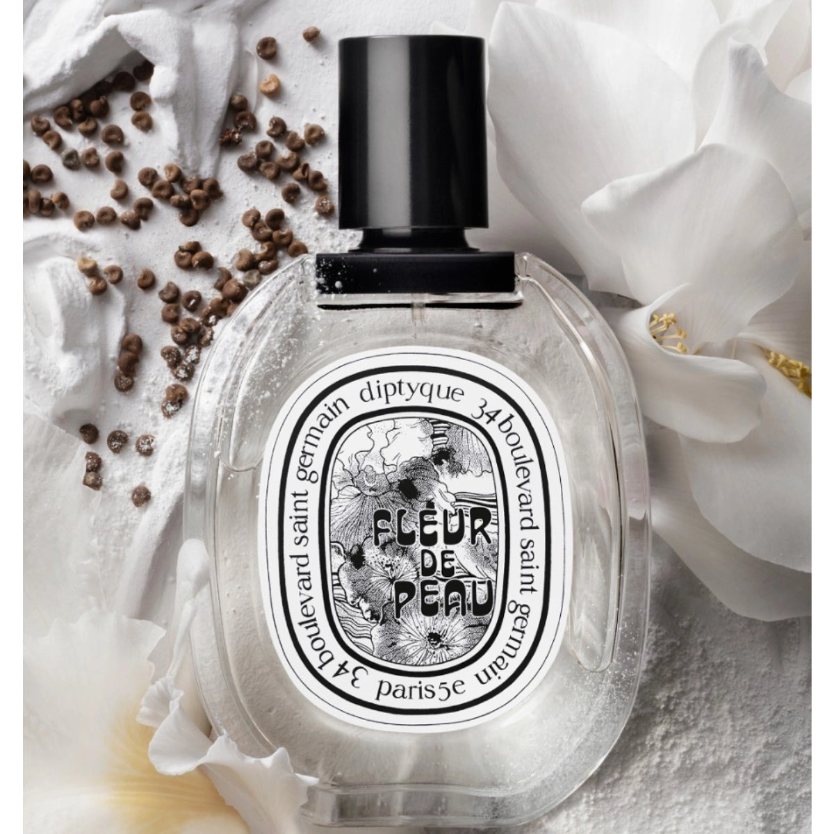 Diptyque - Fleur de Peau - Eau de Toilette in elegantem Flakon umgeben von weißen Blüten und braunen Samen auf hellem Untergrund
