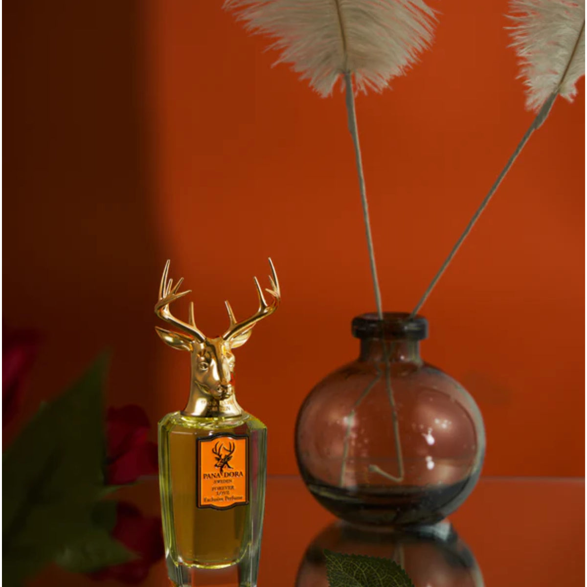 Pana Dora Sweden - Forever Love zeigt Flakon mit goldenem Hirschkopf vor warmem, orangefarbenem Hintergrund