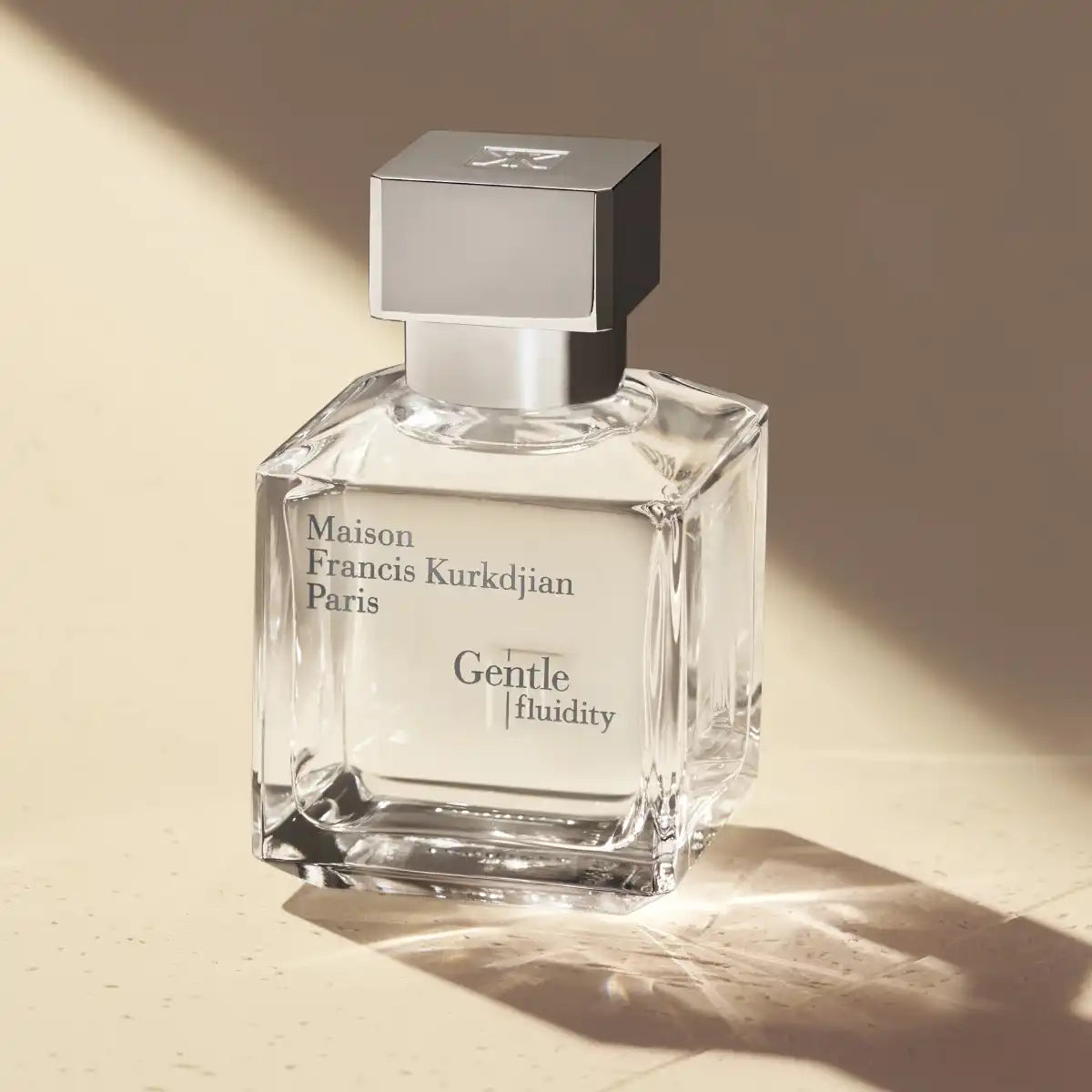 Maison Francis Kurkdjian Paris - Gentle fluidity Silver transparenter Flakon mit silbernem Verschluss vor beigem Hintergrund