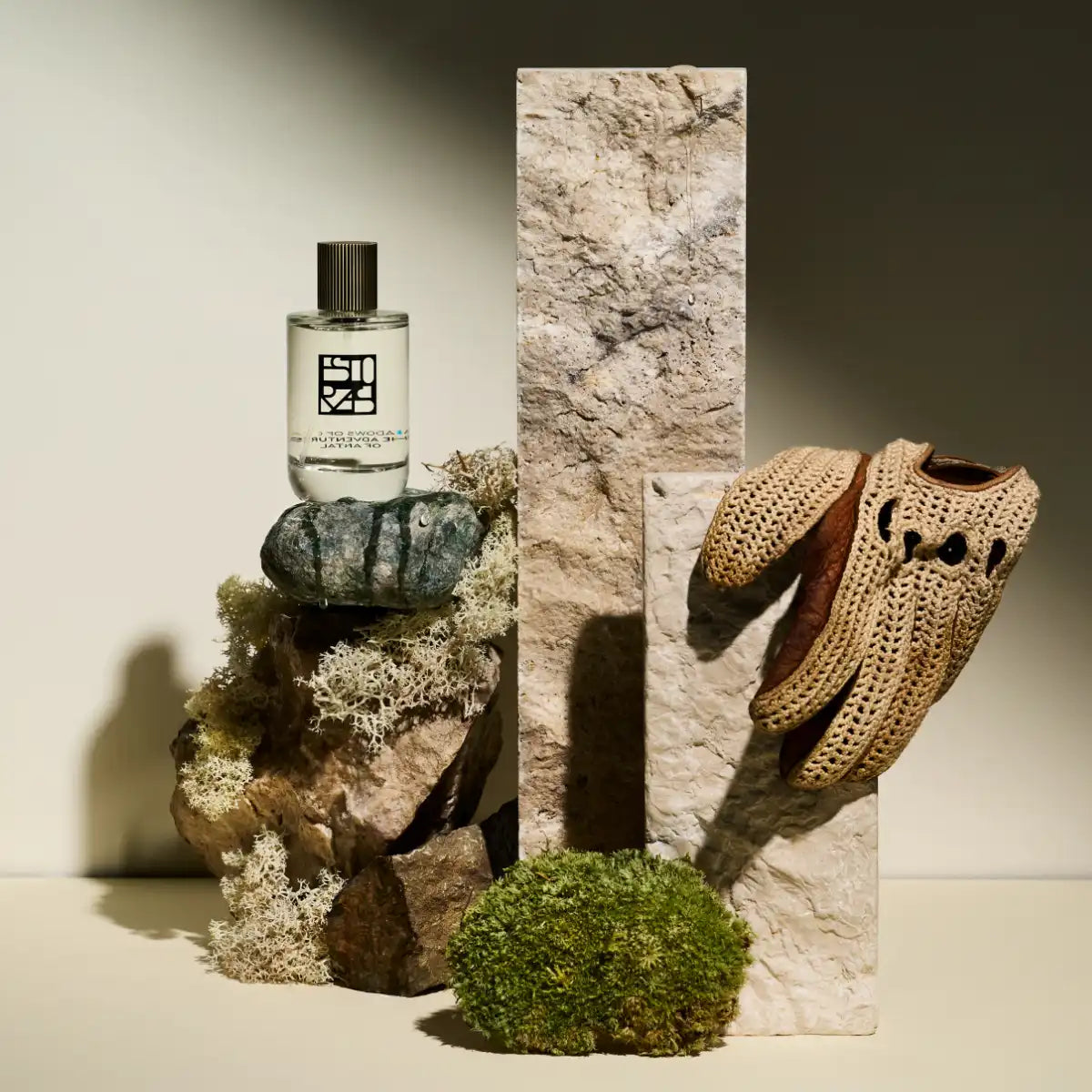 Estoras - Shadows of Giza Parfumflakon auf Naturstein mit Moos und handgestricktem Handschuh vor neutralem Hintergrund