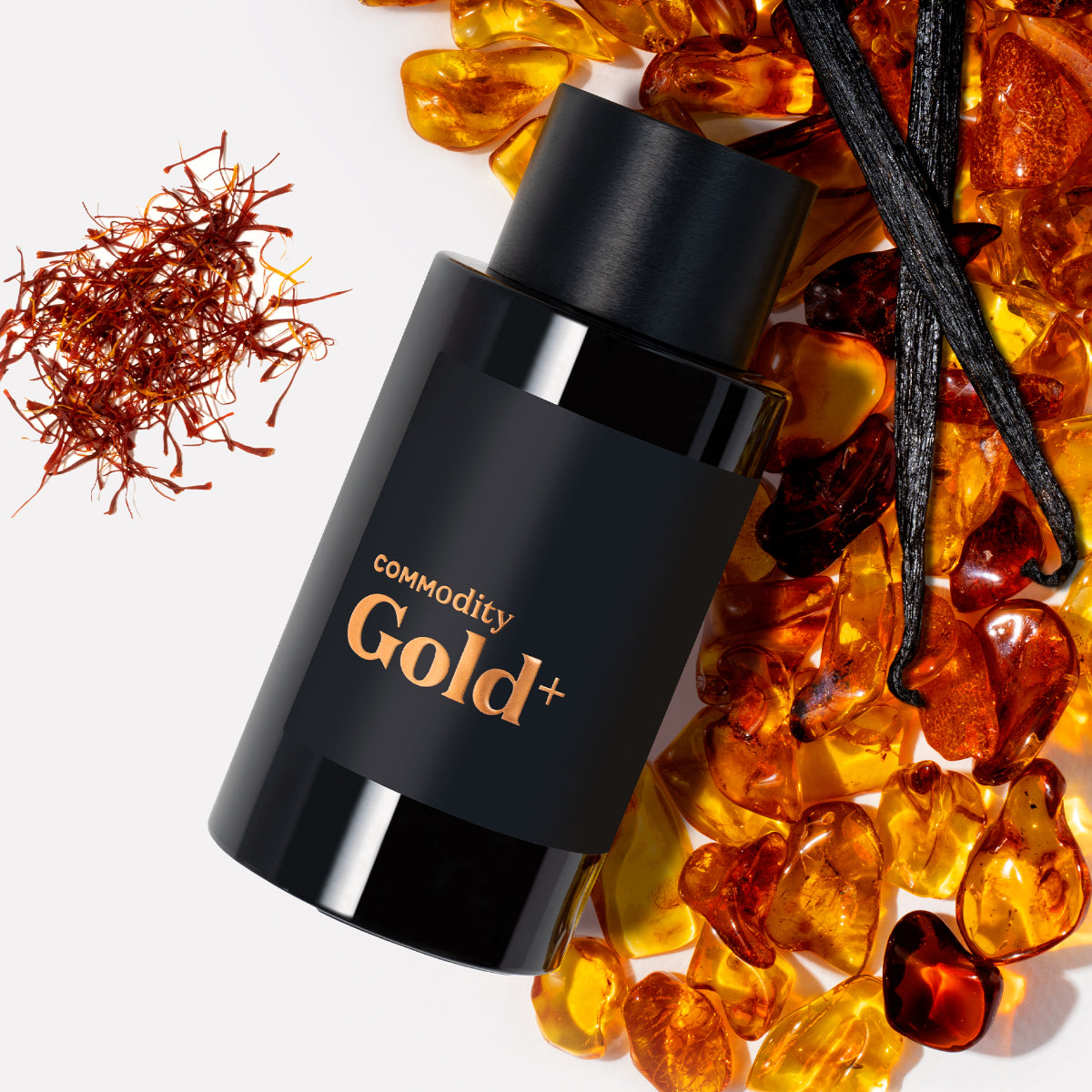 Commodity - Gold+ schwarzer Flakon mit goldfarbenem Schriftzug umgeben von Bernstein, Vanilleschoten und Safranfäden