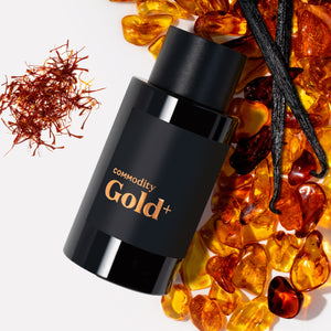 Commodity - Gold+ schwarzer Flakon mit goldfarbenem Schriftzug umgeben von Bernstein, Vanilleschoten und Safranfäden