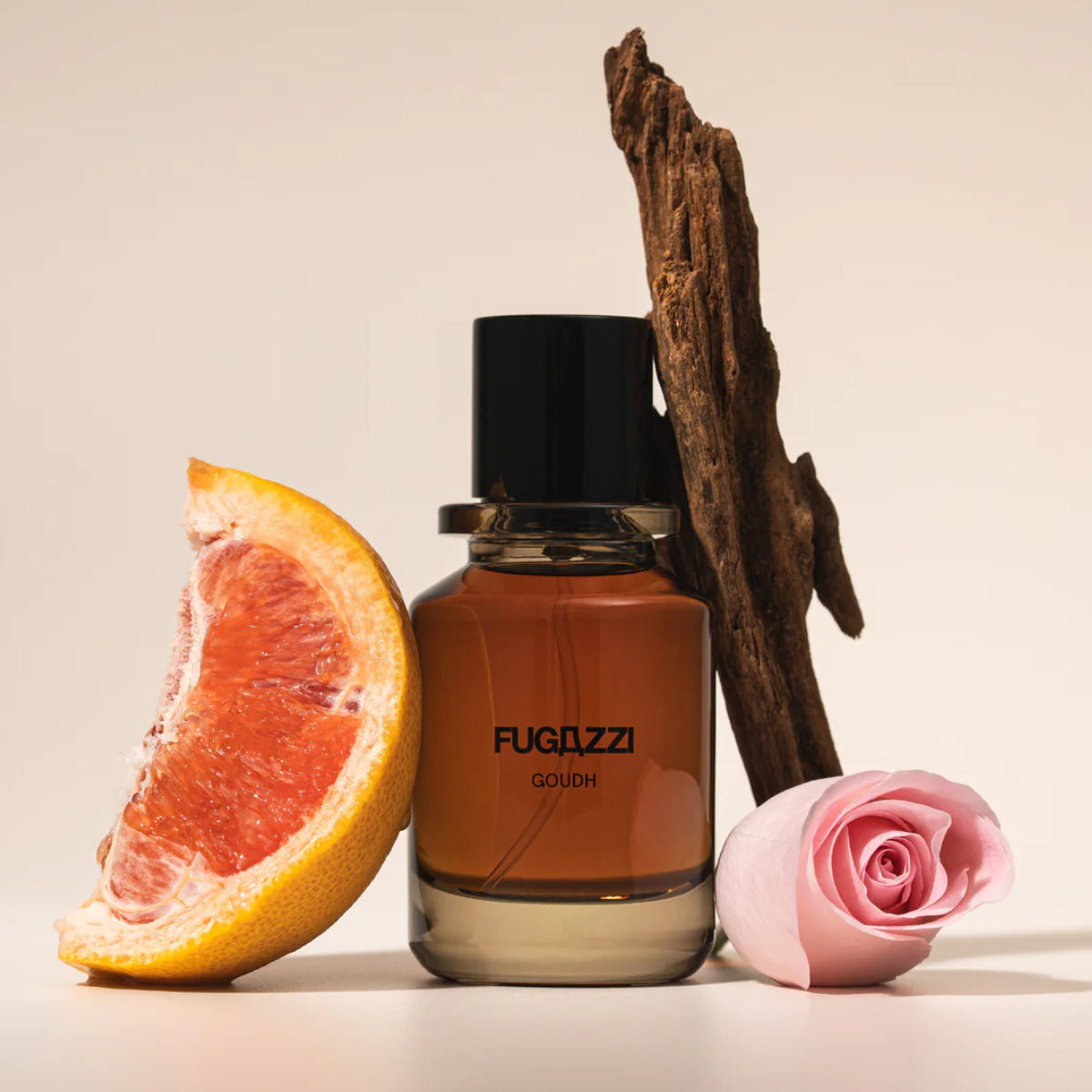 Fugazzi - Goudh Parfumflakon mit warmem Duft vor Grapefruit, Rosenblüte und Holzstück vor hellem Hintergrund