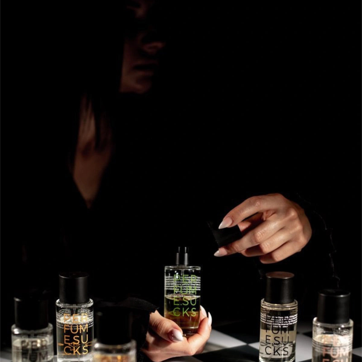 PERFUME.SUCKS - Green 368C Parfumflakon mit schwarzem Deckel und neongrüner Schrift im dunklen Ambiente vor Person mit Hand