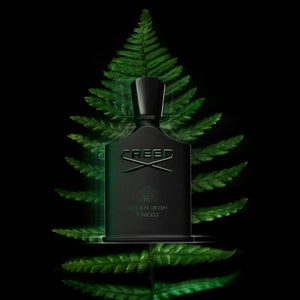 Creed - Green Irish Tweed Parfumflakon mit mattschwarzem Design vor grünem Farnblatt auf schwarzem Hintergrund