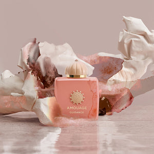 Amouage - Guidance - Hair Perfume in elegantem rosa Flakon vor zarten, künstlerischen Stoffformen und pudrigem Hintergrund