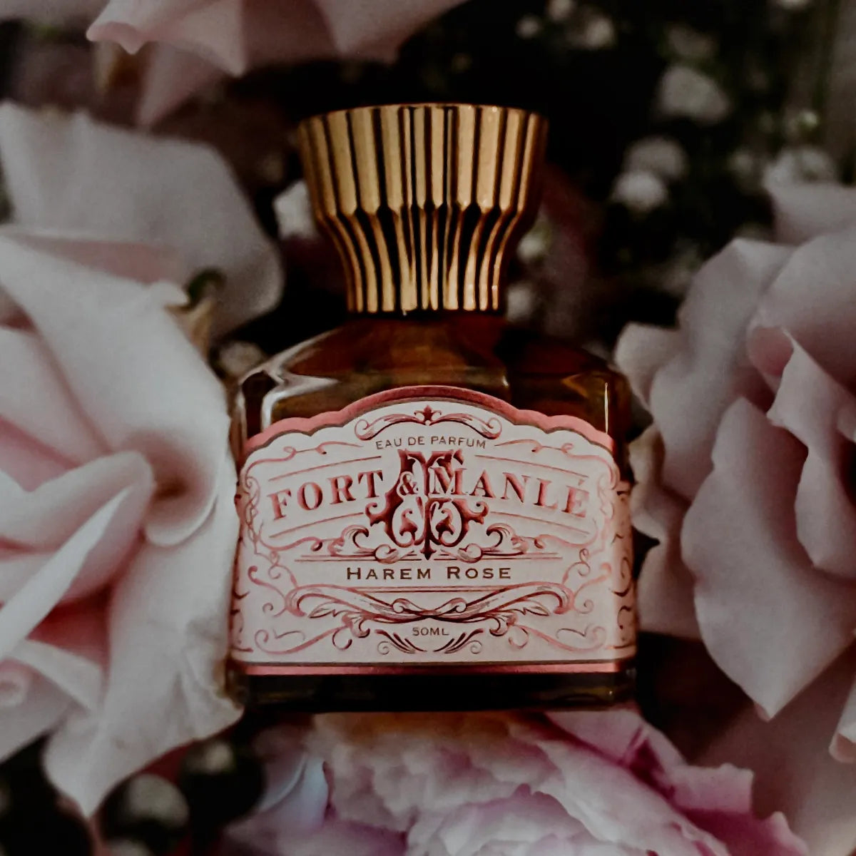 Fort & Manlé - Harem Rose Parfümflakon mit zartrosa Ornamenten und goldfarbenem, elegant gerilltem Verschluss umgeben von Rosenblüten