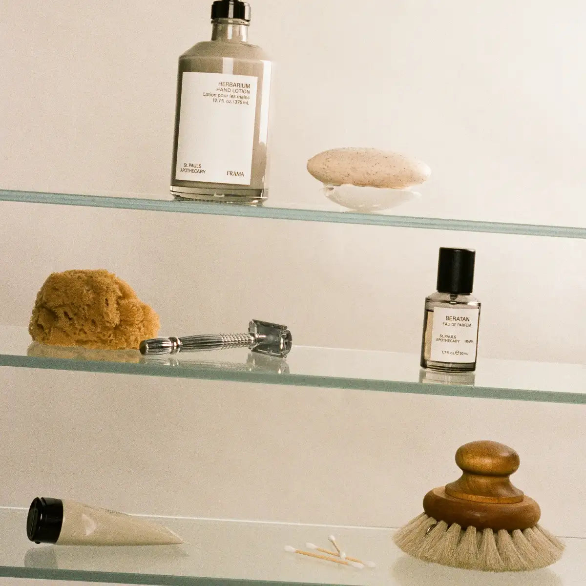 FRAMA - Herbarium - Hand Lotion in schlichtem Glasflakon mit schwarzem Verschluss auf Glasregal mit Naturkosmetikmaterialien