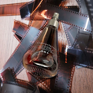 Nomenclature - holy_wood Parfumflakon in tropfenförmigem Glas mit silbernem Zerstäuber auf Holz und Filmstreifen