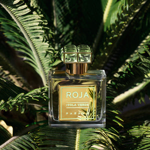 Roja Parfums - Isola Verde Parfumflakon mit goldfarbenem Etikett auf tropischem Blattwerk in natürlichem Licht