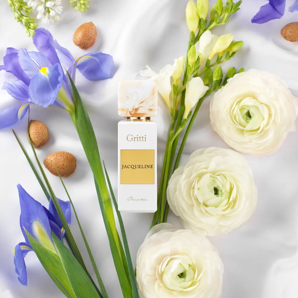 Gritti - White Collection - Jacqueline eleganter Flakon mit goldfarbenem Label umgeben von Frühlingsblumen auf weißem Stoff