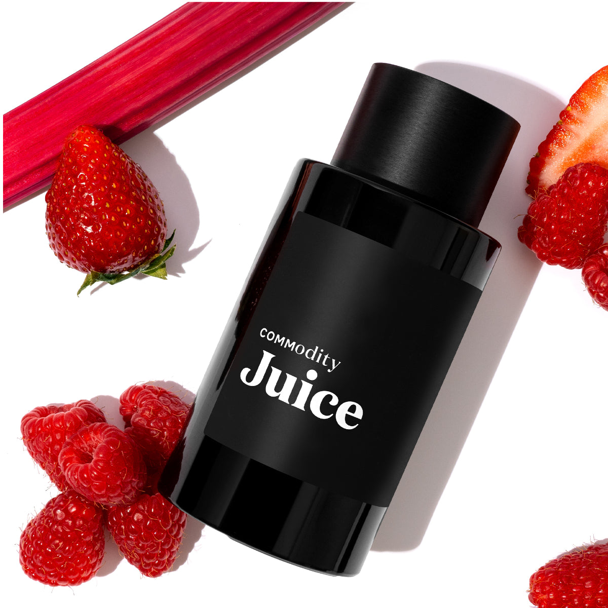 Commodity - Juice schwarzer Flakon mit weißem Schriftzug umgeben von frischer Erdbeere, Himbeeren und Rhabarberstange