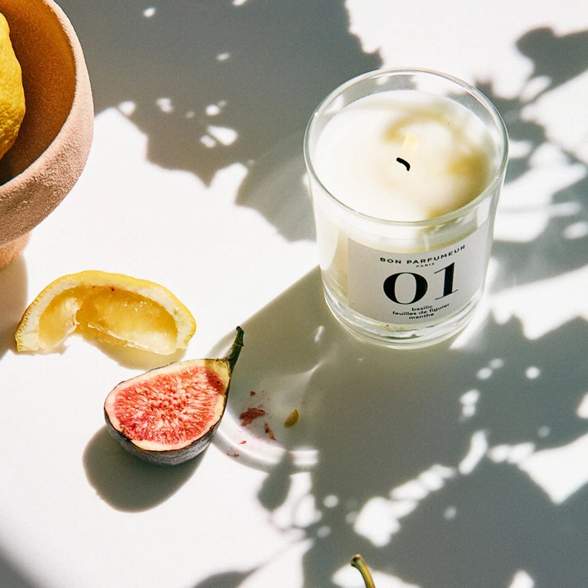 Bon Parfumeur - Candle 01 mit schlichter Glasform, Zitronenscheibe und halbierter frischer Feige im Sonnenlicht