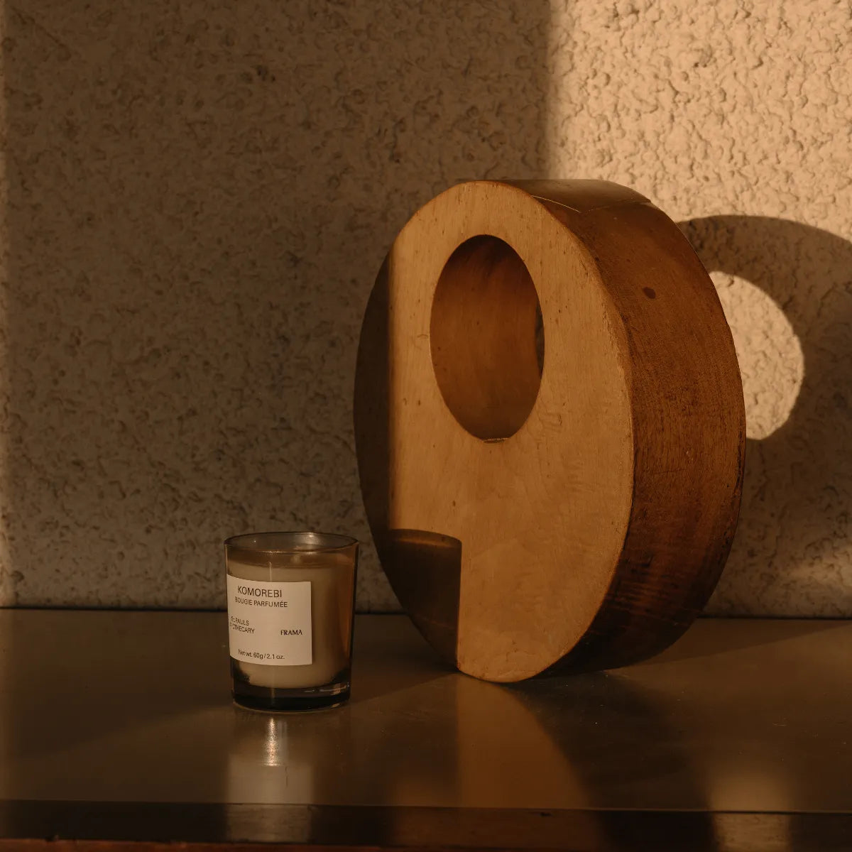 FRAMA - Komorebi - Duftkerze in klarem Glas neben abstrakter Holzskulptur im warmen, natürlichem Lichtspiel
