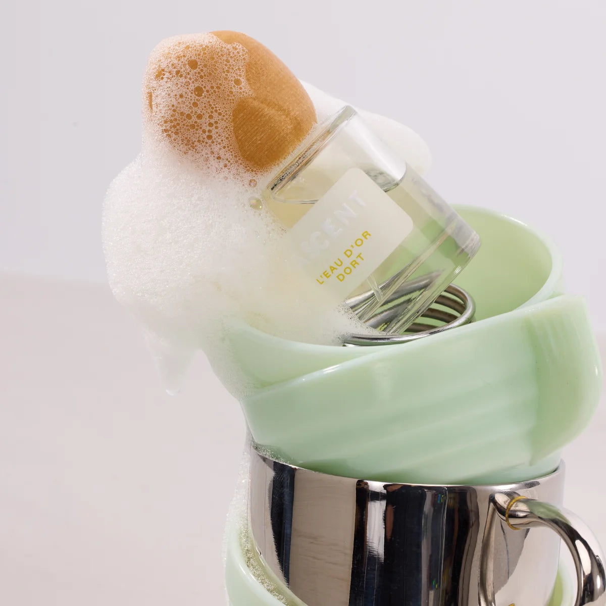 Fascent - L'Eau d'Or Dort Flakon mit schaumigem Badeschaum in pastellgrüner Schale und silbernem Becher