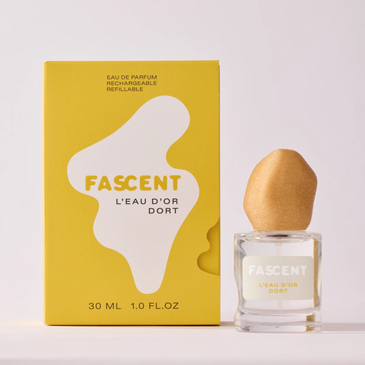 Fascent - L'Eau d'Or Dort Parfumflakon mit organisch geformtem Deckel und gelber Verpackung auf weißem Hintergrund