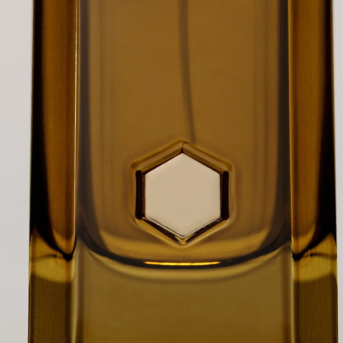 D:SOL MMXVI - Ládano Flakon in bernsteinfarbenem Glas mit geometrischem sechseckigem Detail auf hellem Hintergrund
