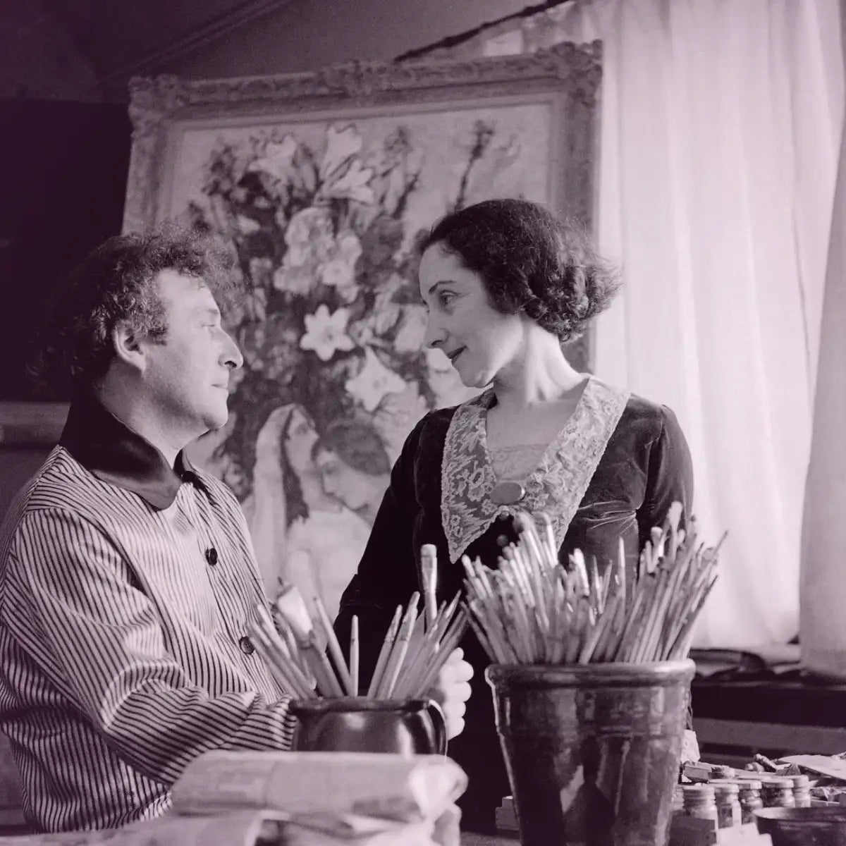 Cherigan - Lovers in Pink zeigt ein Künstlerpaar im Atelier vor einem blumigen Gemälde in nostalgischer Schwarz-Weiß-Atmosphäre
