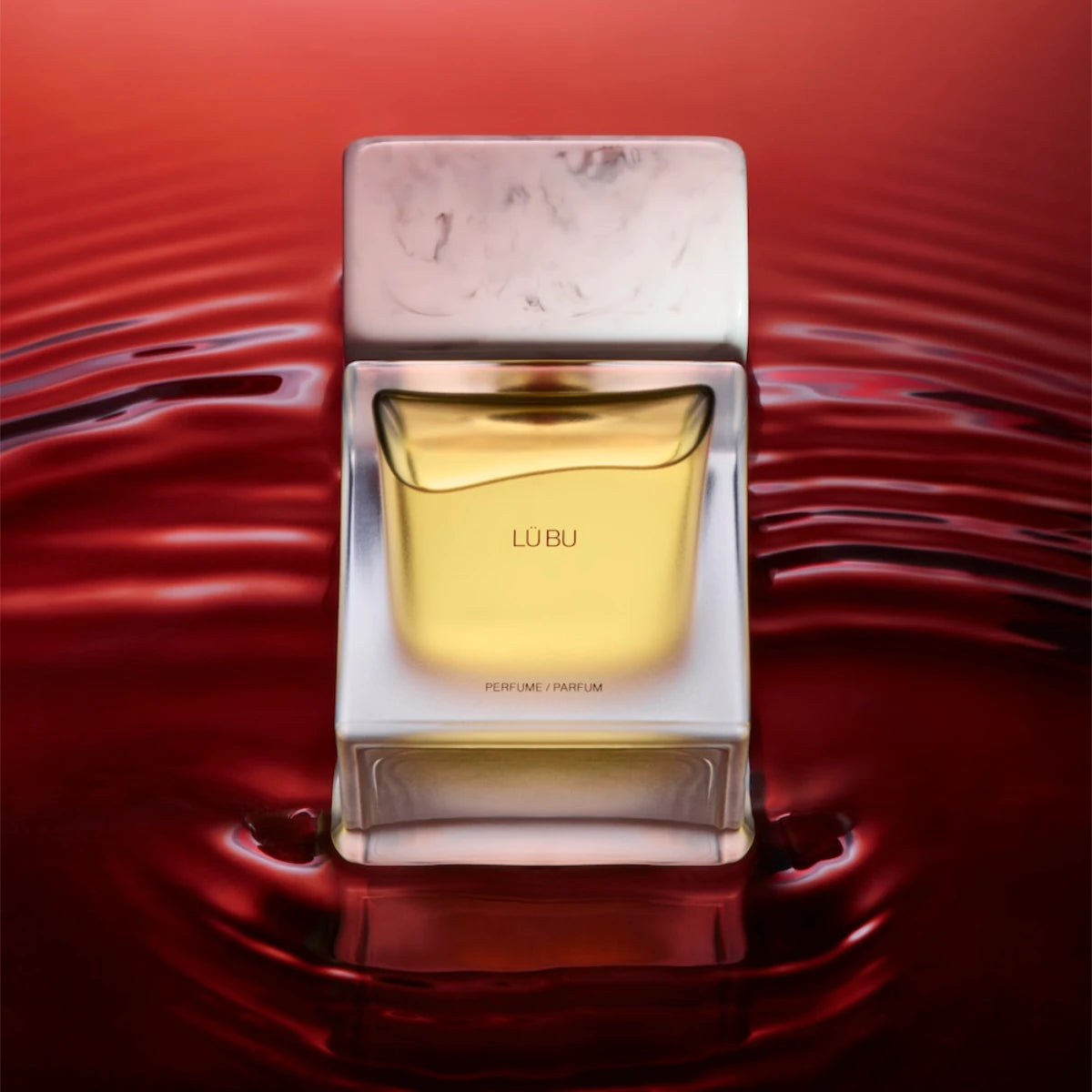 Sora Dora - White Collection - Lü Bu Parfumflakon mit bernsteinfarbener Flüssigkeit vor rotem, wellenförmigem Hintergrund