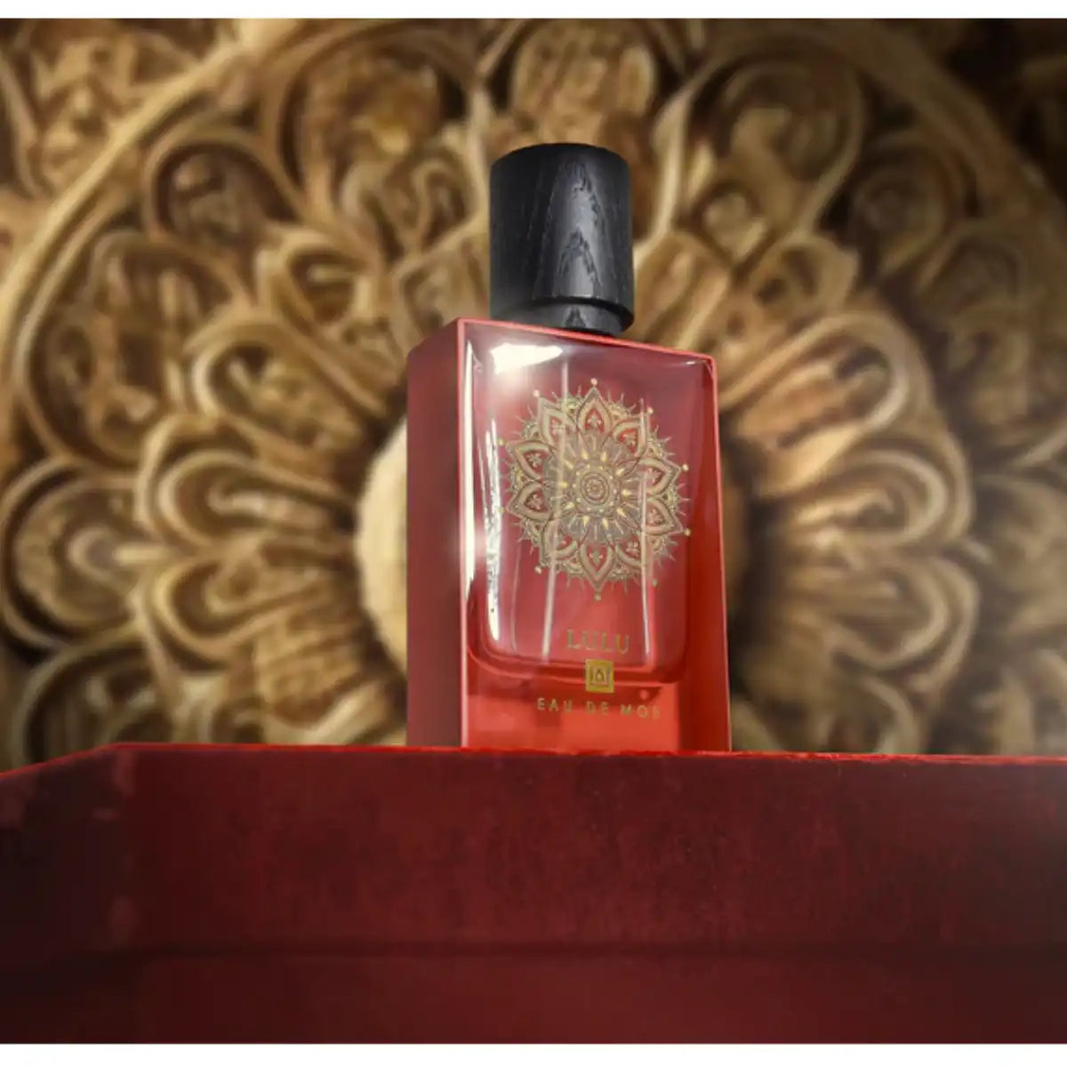 Eau De Moe - Lulu Parfüm in rotem Glas mit goldenem Mandala, schwarzem Verschluss, vor kunstvollem Hintergrund präsentiert