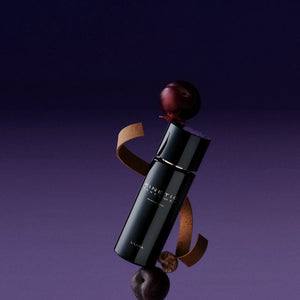 Kinetic Perfumes - L'Una Parfumflakon in glänzendem Schwarz mit elegantem Design vor violettem Hintergrund und Dekoration