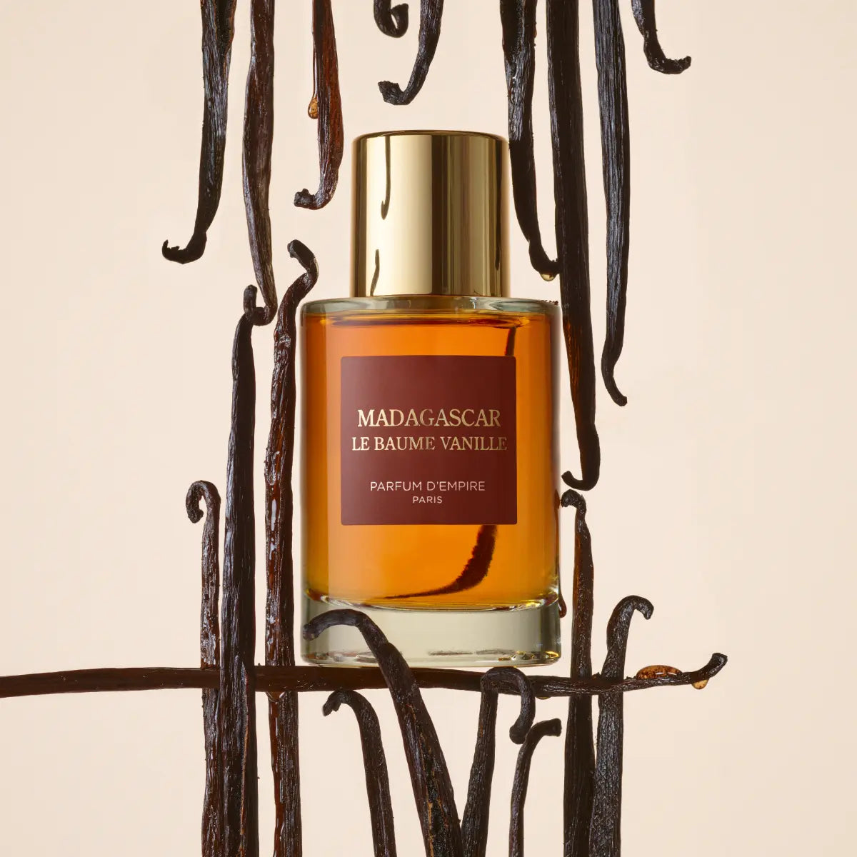 Parfum d'Empire - Madagascar, Le Baume Vanille Flakon mit goldfarbenem Verschluss umgeben von Vanilleschoten vor hellem Hintergrund
