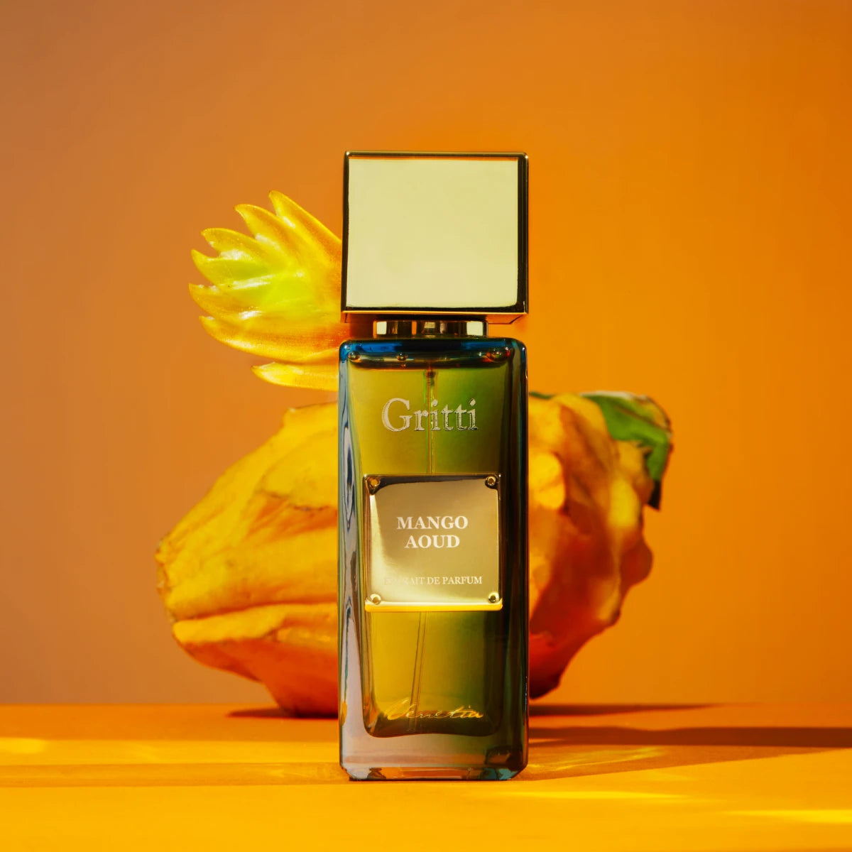 Gritti - Ivy Collection - Mango Aoud Parfumflakon mit goldfarbenem Verschluss vor warmem orangefarbenem Hintergrund