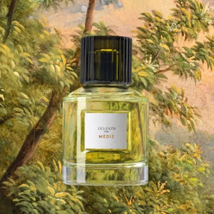 Trudon - Médie Parfumflakon mit klarem Glas und schwarzem Verschluss vor naturalistisch gemaltem Hintergrund