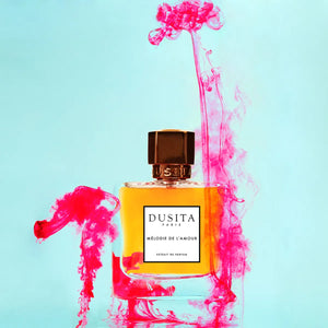 Dusita - Mélodie de l’Amour Parfumflakon mit bernsteinfarbener Essenz umgeben von rosa Tinte vor hellblauem Hintergrund
