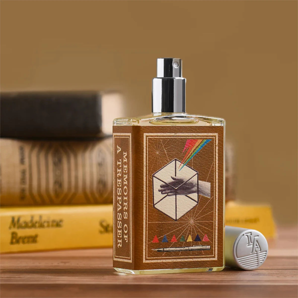 Imaginary Authors - Memoirs of a Trespasser Parfumspray mit kreativem Etikett vor gestapelten Büchern und Holztisch
