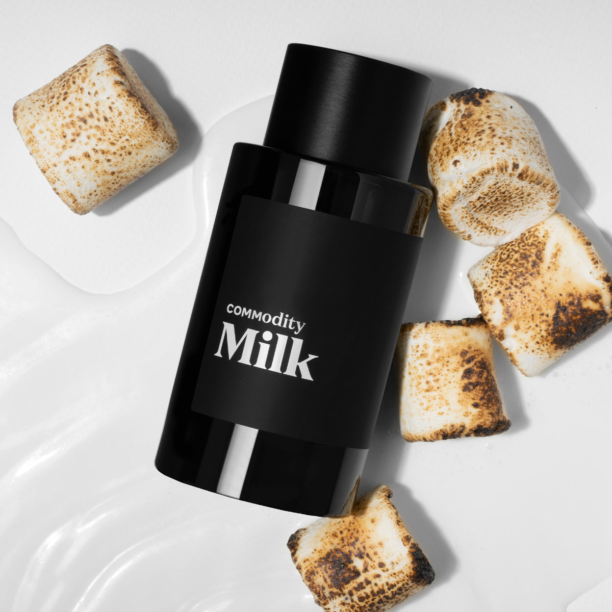 Commodity - Milk Parfumflakon in schwarzem Design umgeben von gerösteten Marshmallows auf weißer Oberfläche präsentiert
