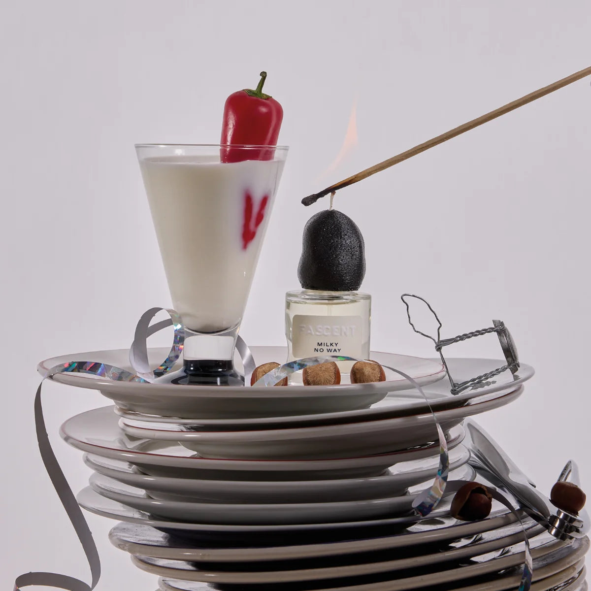 Fascent - Milky No Way Parfumflakon mit schwarzem Deckel neben Milchglas und rotem Paprika auf Tellerstapel
