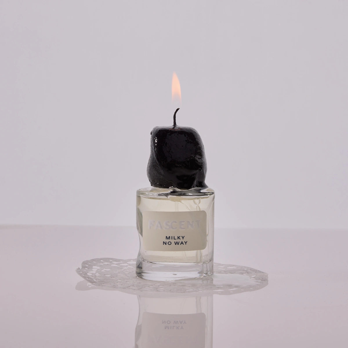Fascent - Milky No Way Parfumflakon mit geschmolzener schwarzer Kerze und Lichtflamme auf spiegelnder Oberfläche