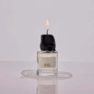 Fascent - Milky No Way Parfumflakon mit geschmolzener schwarzer Kerze und Lichtflamme auf spiegelnder Oberfläche