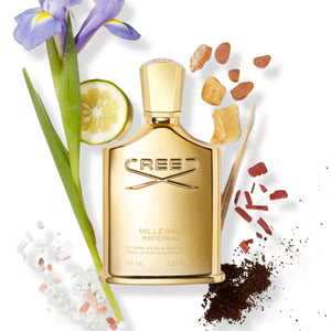 Creed - Millésime Imperial Parfumflakon in goldener Optik umgeben von natürlichen Duftnoten auf weißem Hintergrund