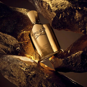 Creed - Millésime Imperial Parfumflakon in goldglänzender Optik zwischen goldfarbenen Steinen auf dunklem Hintergrund