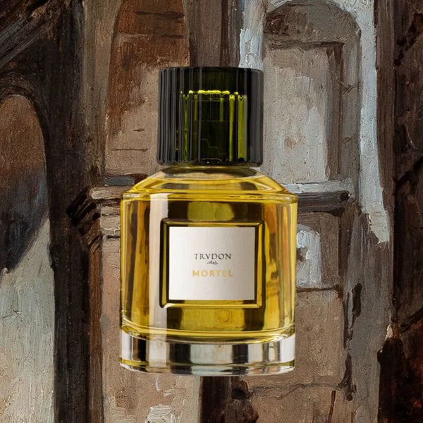 Trudon - Mortel Parfumflakon mit schwarzem Verschluss und goldgelber Flüssigkeit vor rustikalem Hintergrund