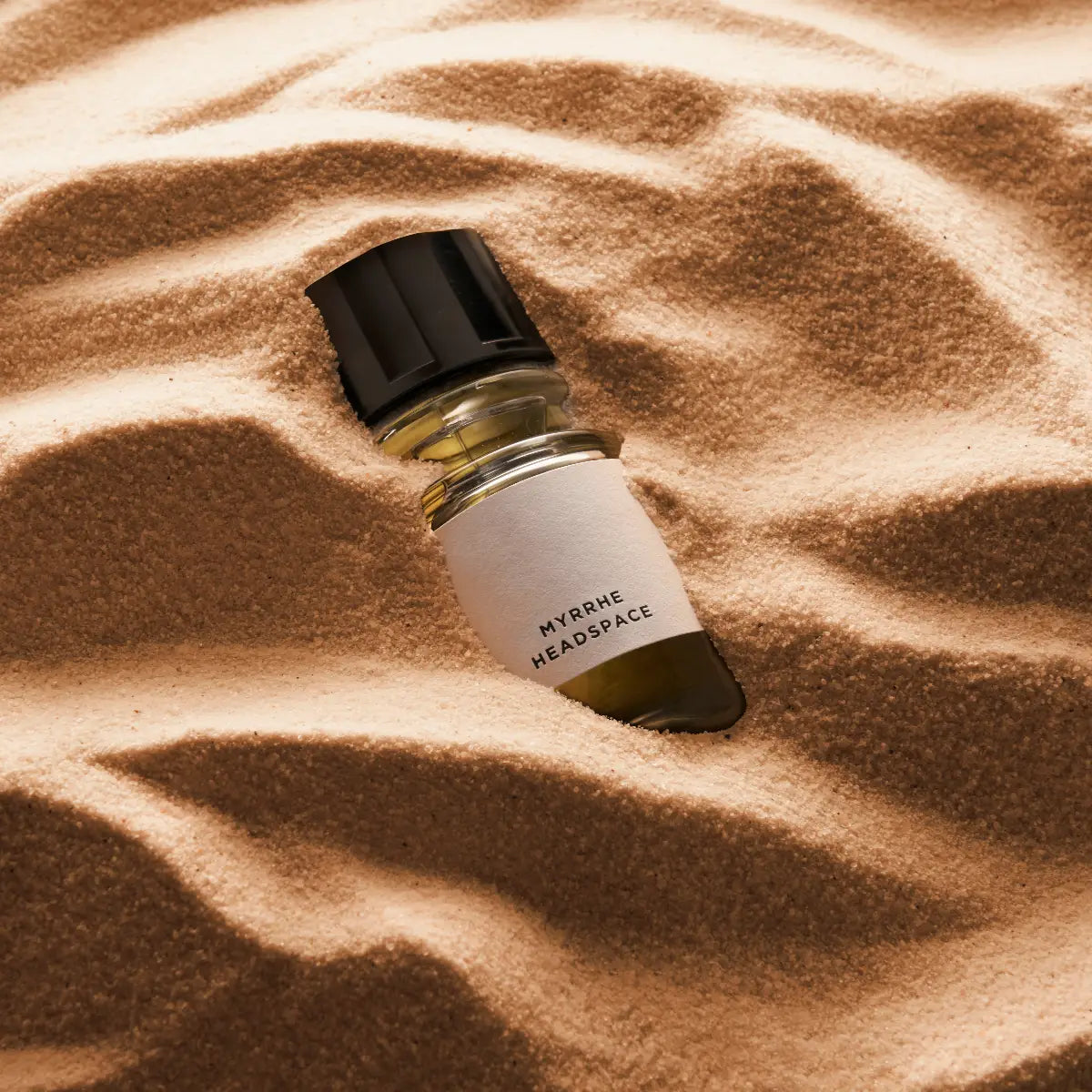 Headspace - Myrrhe Flakon mit bernsteinfarbener Flüssigkeit und schwarzem Verschluss liegt in feinem Sandbett