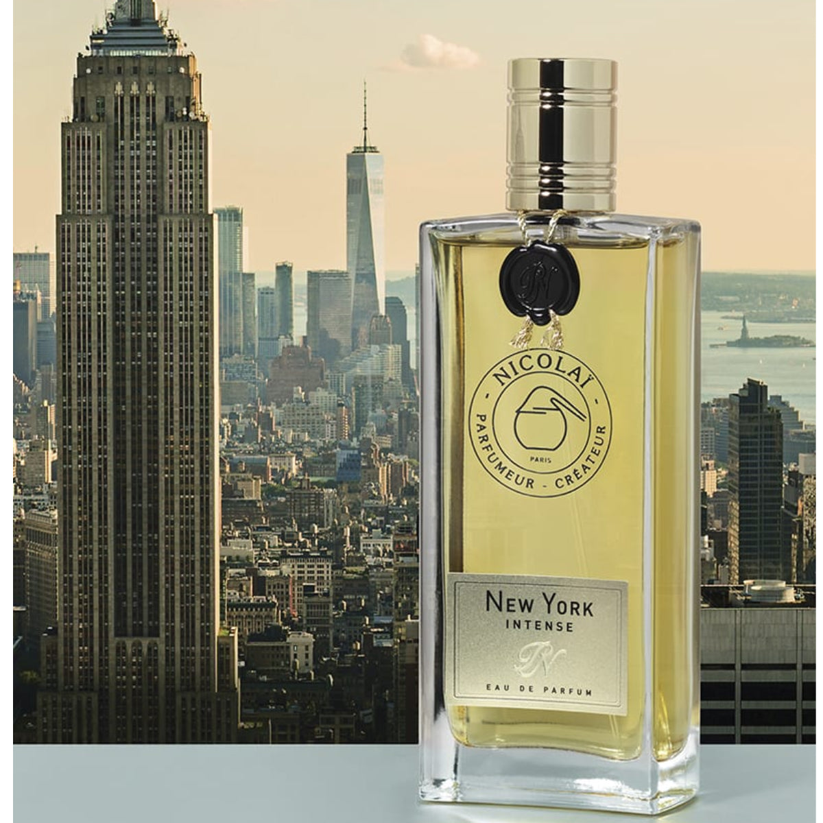 Nicolaï - New York Intense Parfümflakon mit transparentem Glas und silbernem Verschluss vor Stadtpanorama von New York
