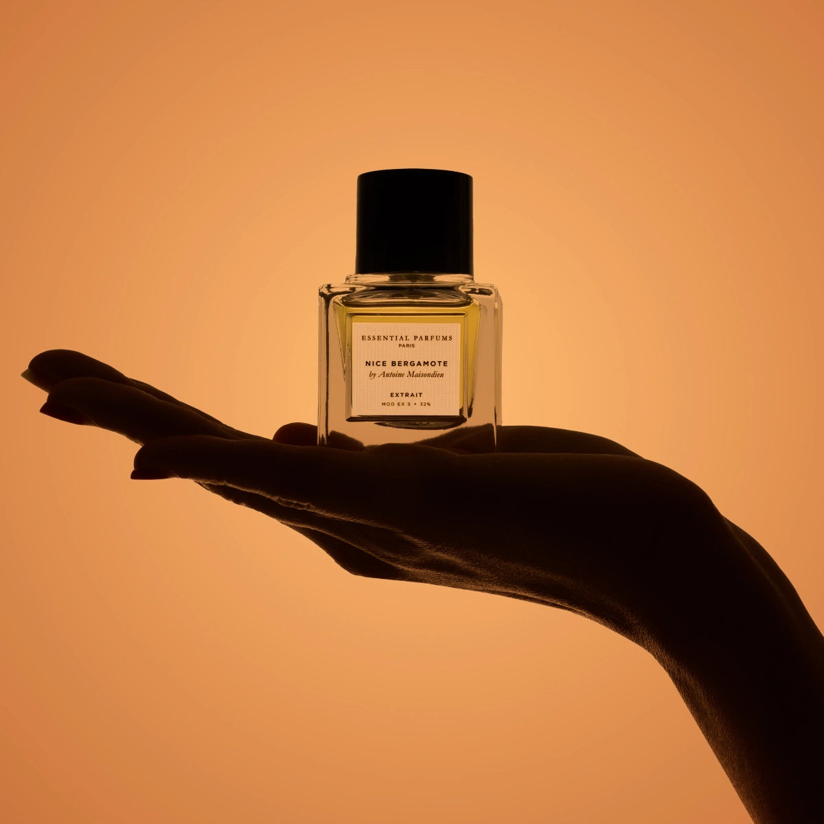 Essential Parfums - Nice Bergamote - Extrait de Parfum präsentiert in handgehaltener Silhouette vor warmem orangem Hintergrund